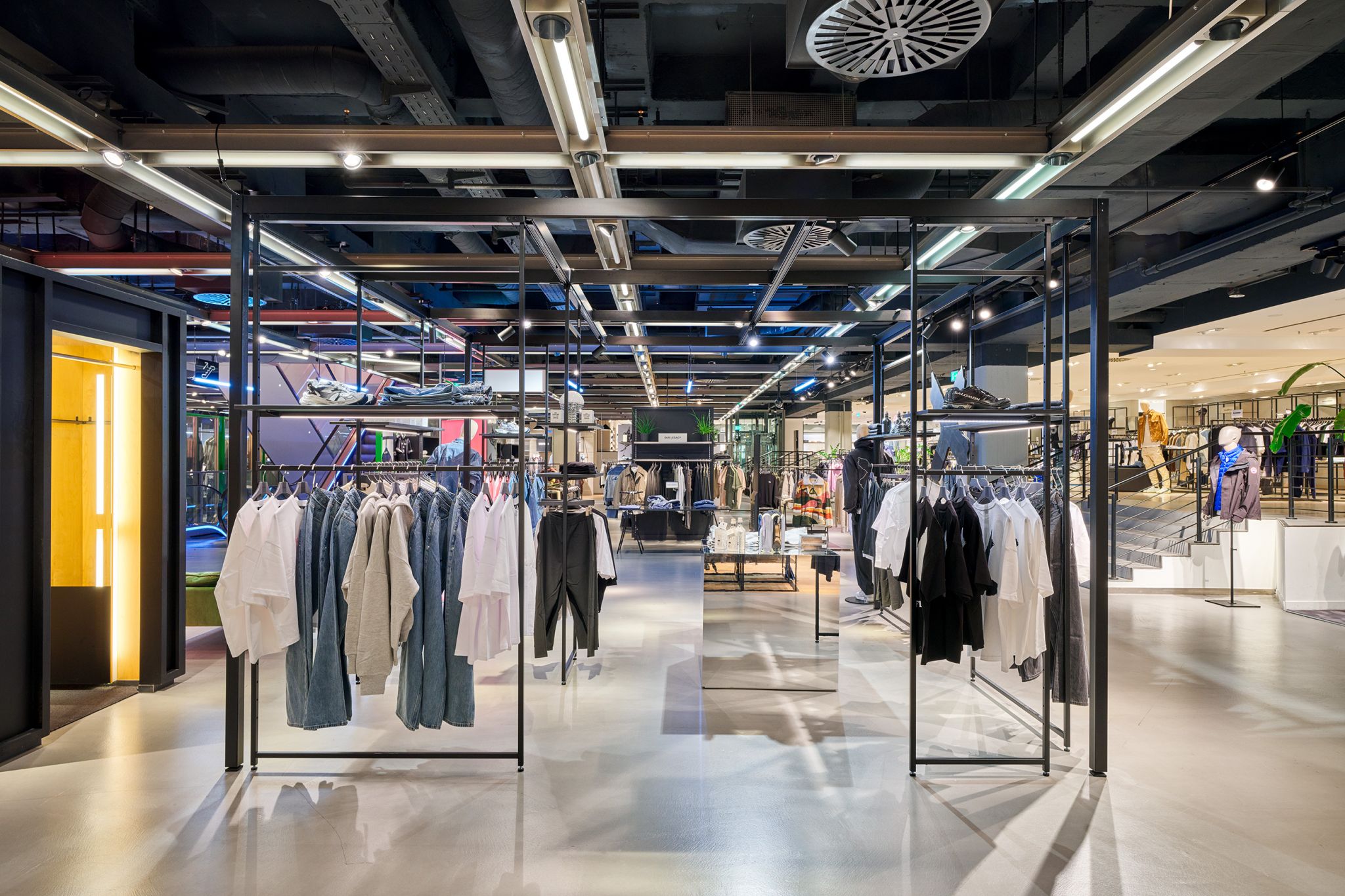 Freistehendes schwarzes Metallstruktursystem mit h&auml;ngender Kleidung in einem modernen Modegesch&auml;ft