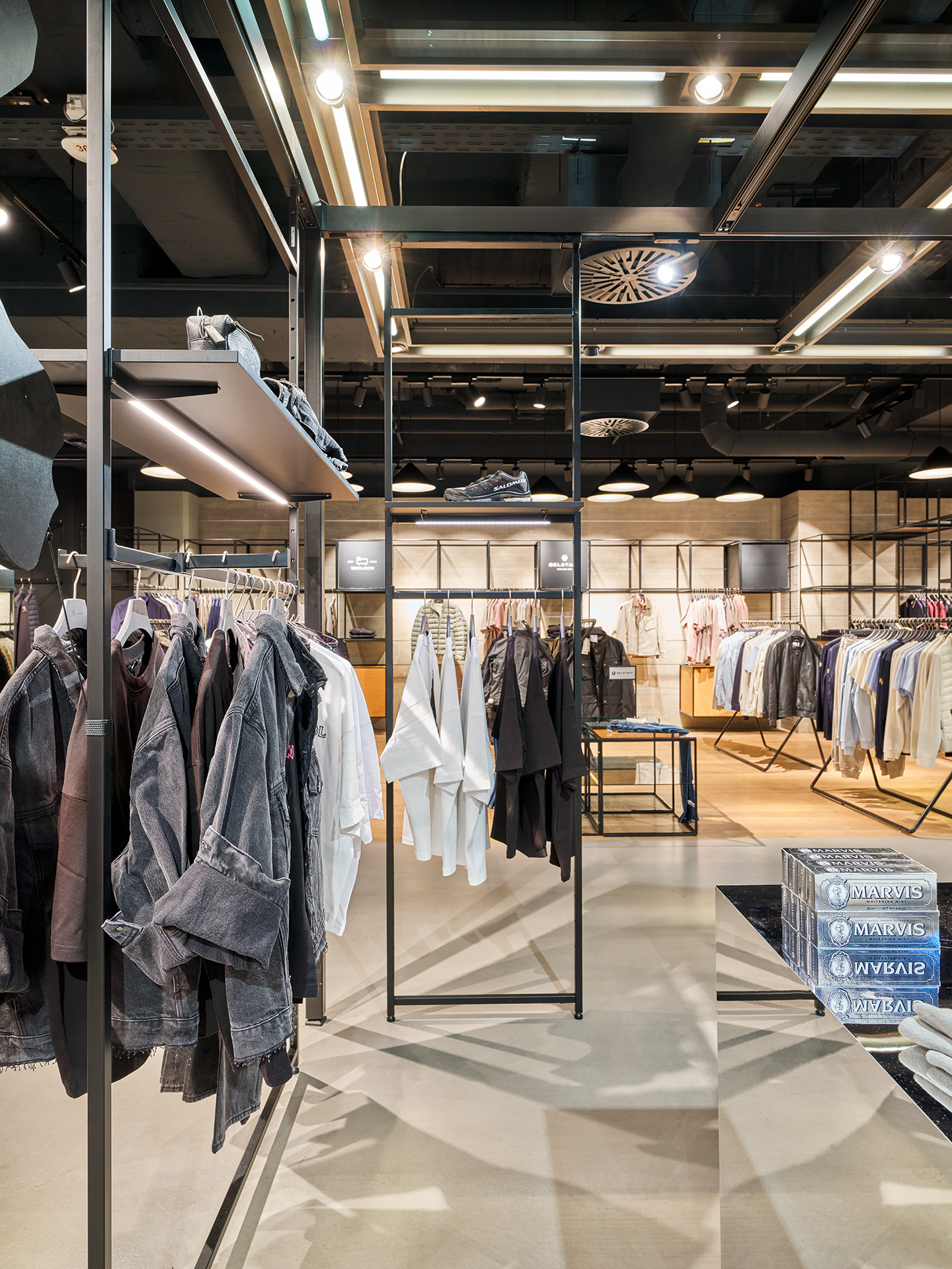 Beleuchtete Regale mit h&auml;ngender Kleidung und Schuhen in einem modernen Bekleidungsgesch&auml;ft