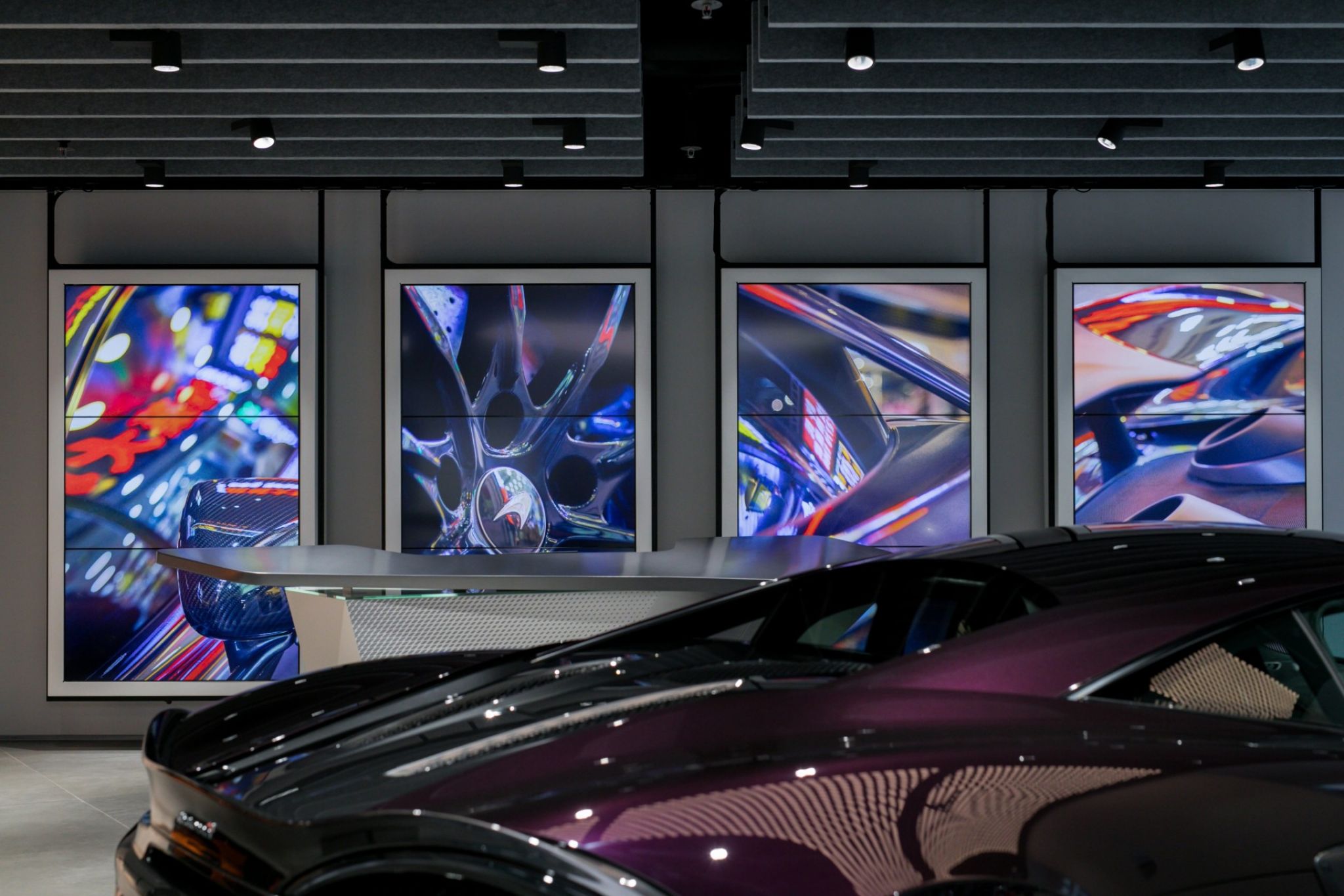 Innenraum einer Gesch&auml;ftsfl&auml;che des Automobilherstellers McLaren mit einem Sportwagen im Vordergrund und von der Decke h&auml;ngenden Displays.