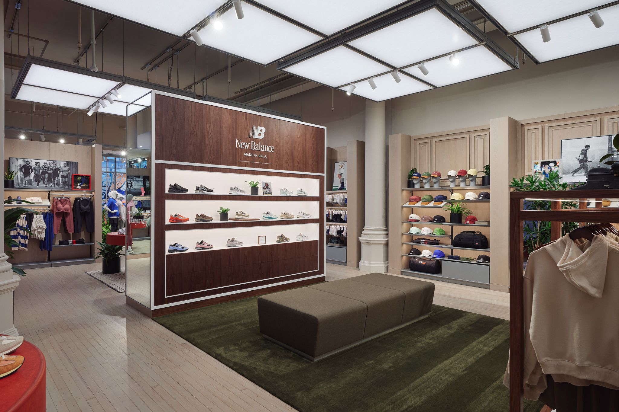Interior de una tienda New Balance con estanter&iacute;as iluminadas con zapatos, percheros con ropa y un banco sobre una alfombra verde.