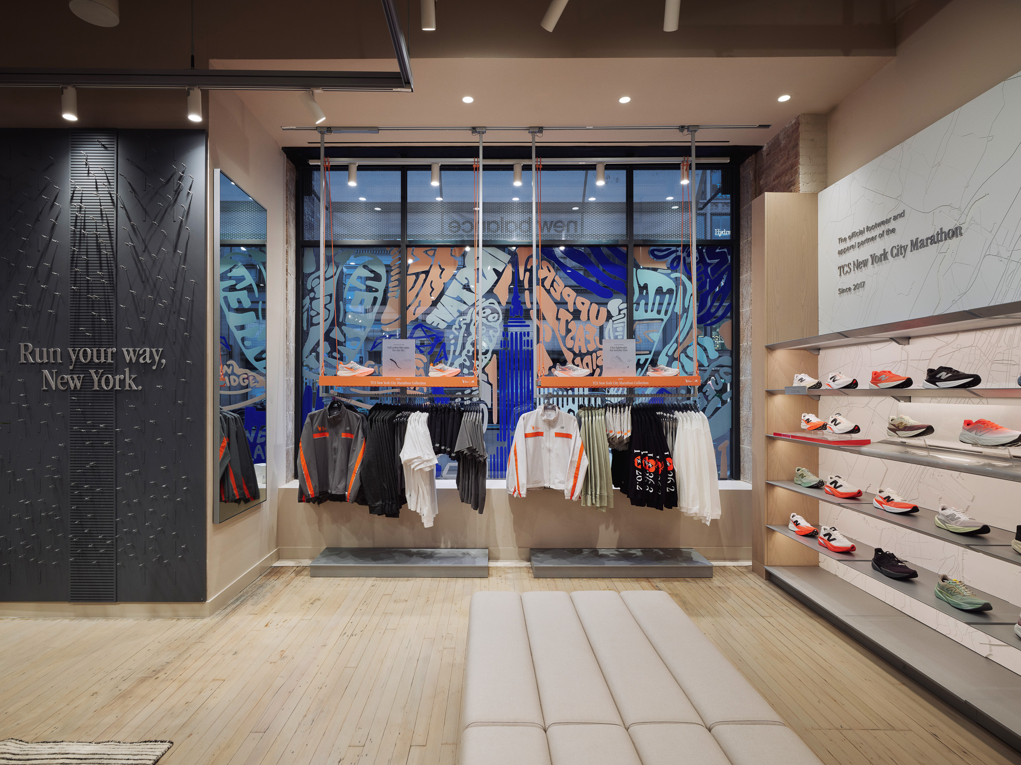 Interior de una tienda deportiva con ropa de correr, estantes de zapatos y texto en la pared 'Run your way, New York.'