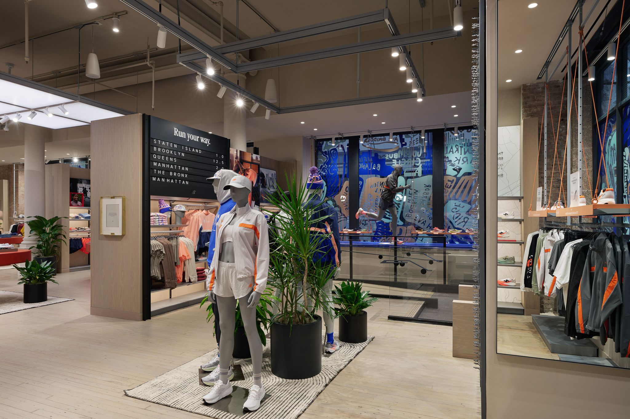 Dos maniqu&iacute;es con ropa deportiva junto a plantas verdes en una tienda de ropa con suelos de madera clara y luces en el techo.