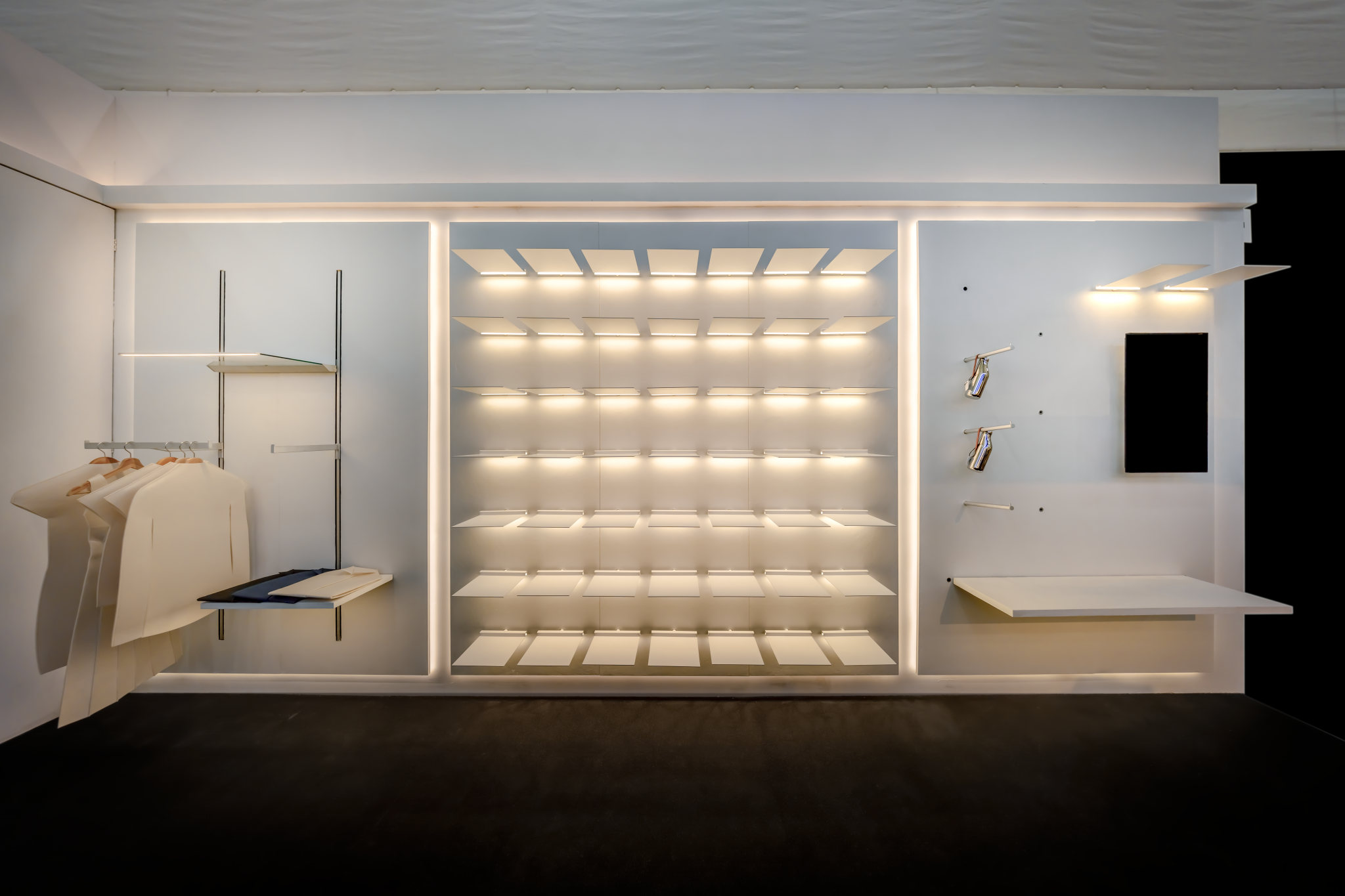 Minimalist wall system with illuminated empty shelves and clothing rods holding a few white garments