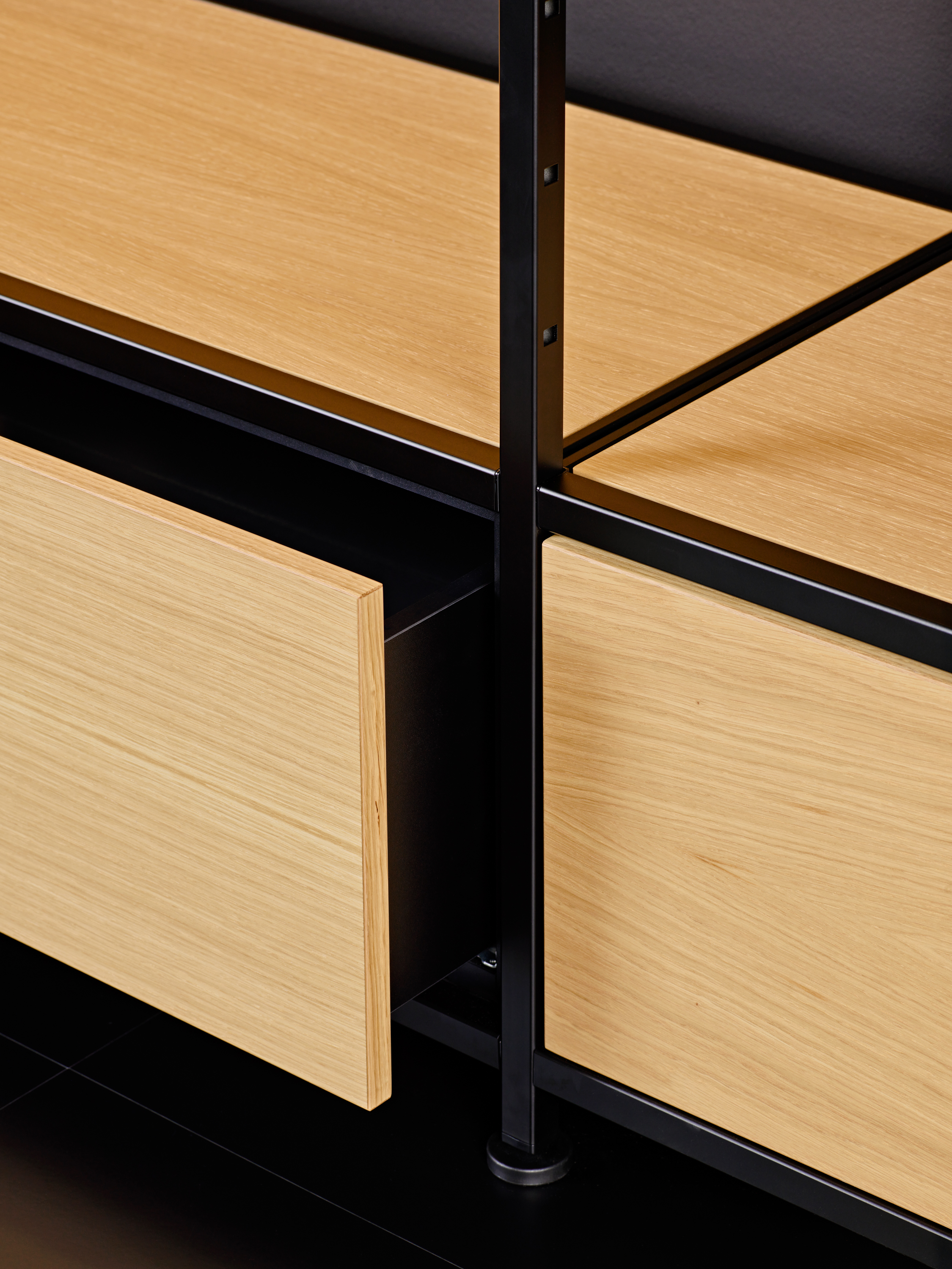 Close-up of an open drawer made of light wood with a black metal frame.