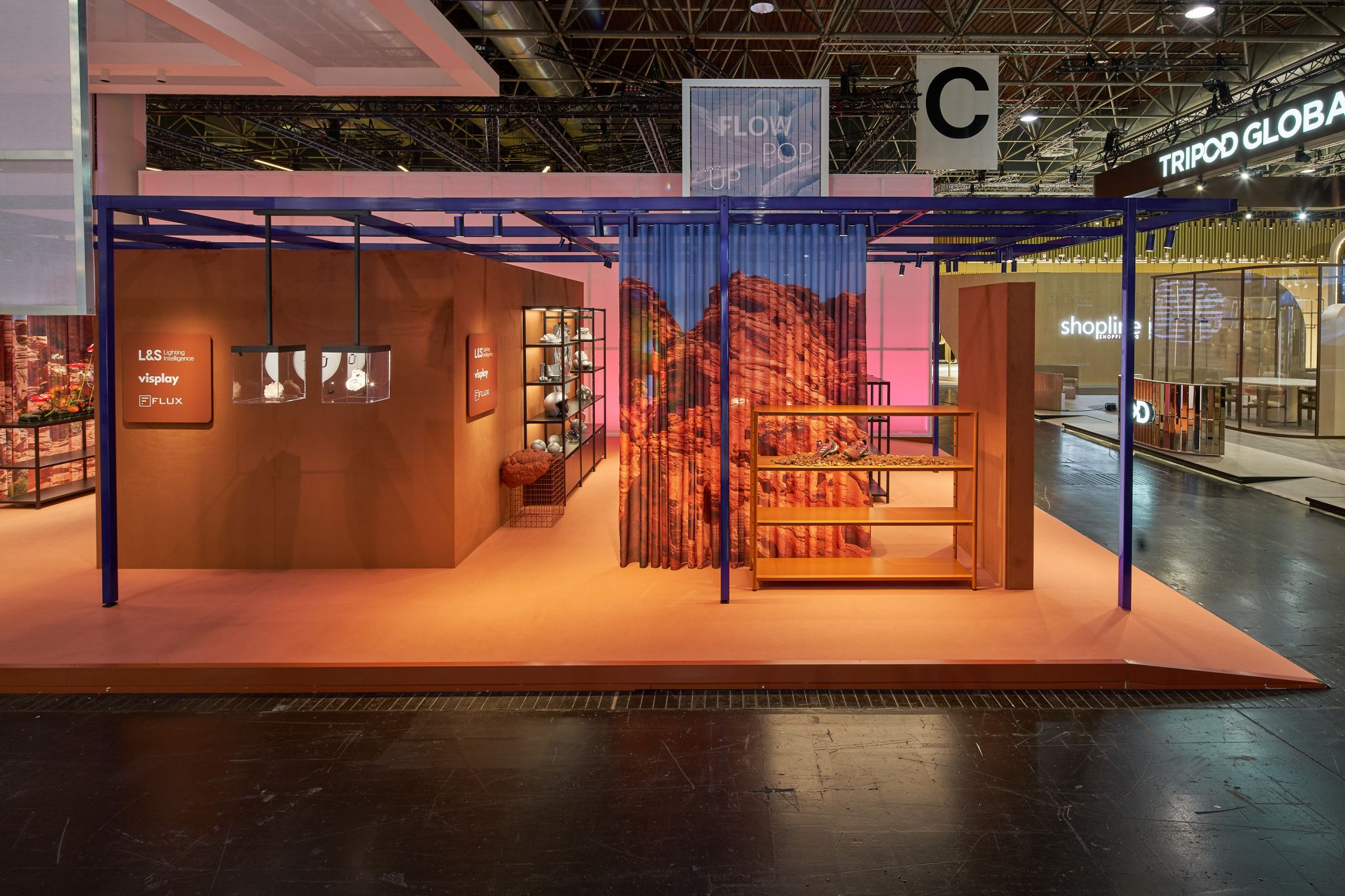 Stand d'exposition avec sol et murs orange, structure en acier bleue, &eacute;tag&egrave;res et rideau avec image de paysage