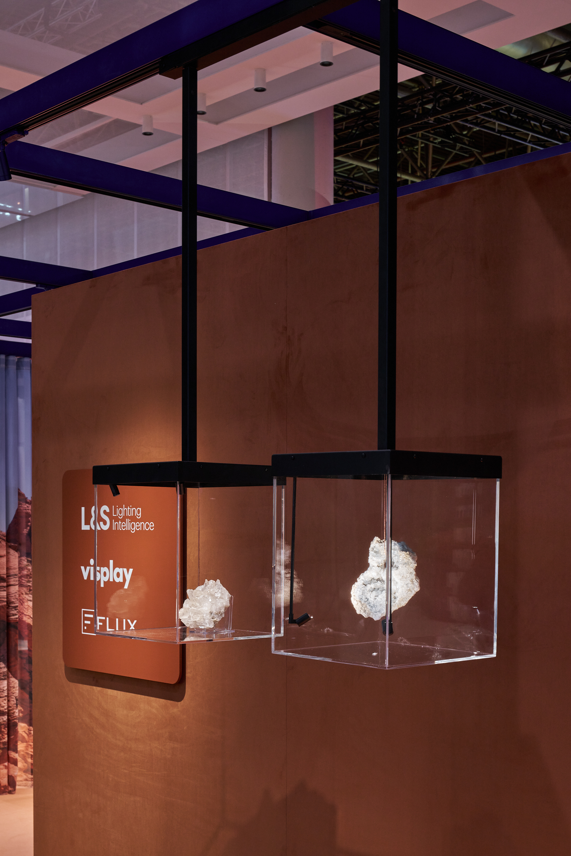 Deux vitrines suspendues en verre contenant une d&eacute;coration blanche devant un mur marron avec les logos L&amp;S Lighting Intelligence, Visplay et FLUX