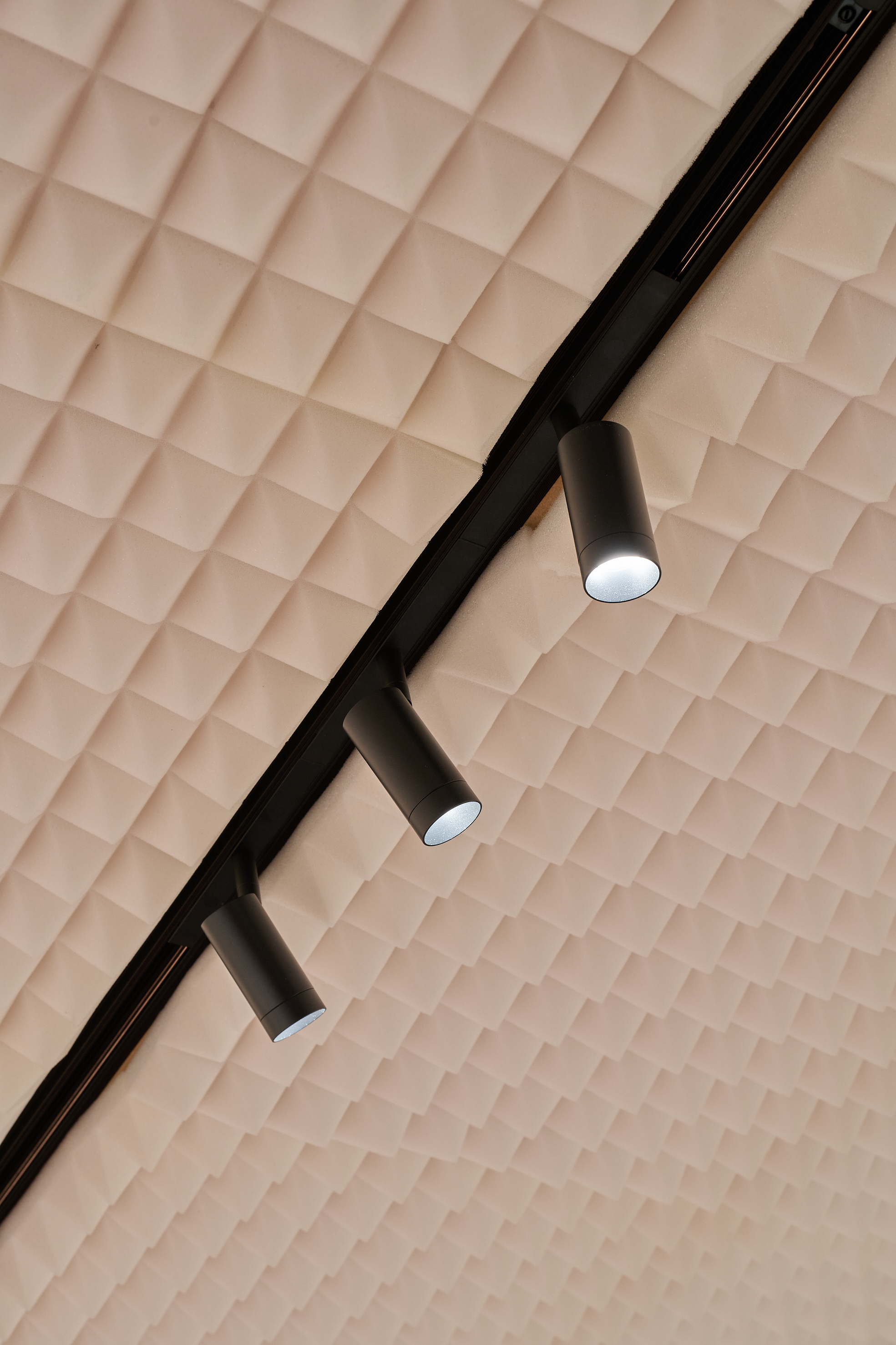 Trois spots de plafond noirs sur une rampe devant un plafond textur&eacute; &agrave; motif carr&eacute;