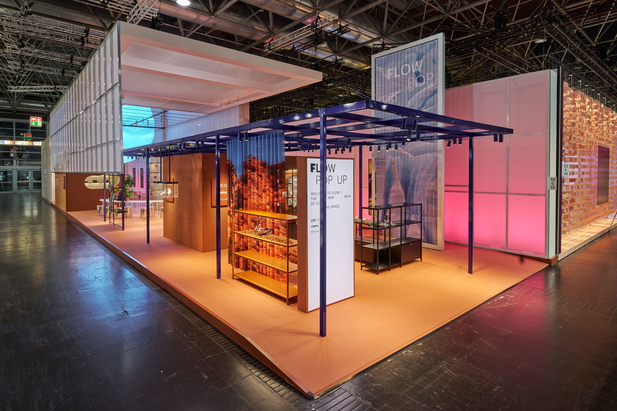 Stand d'exposition &agrave; structure modulaire ouverte avec murs &eacute;clair&eacute;s et &eacute;tag&egrave;res pr&eacute;sentant des produits dans un hall d'exposition