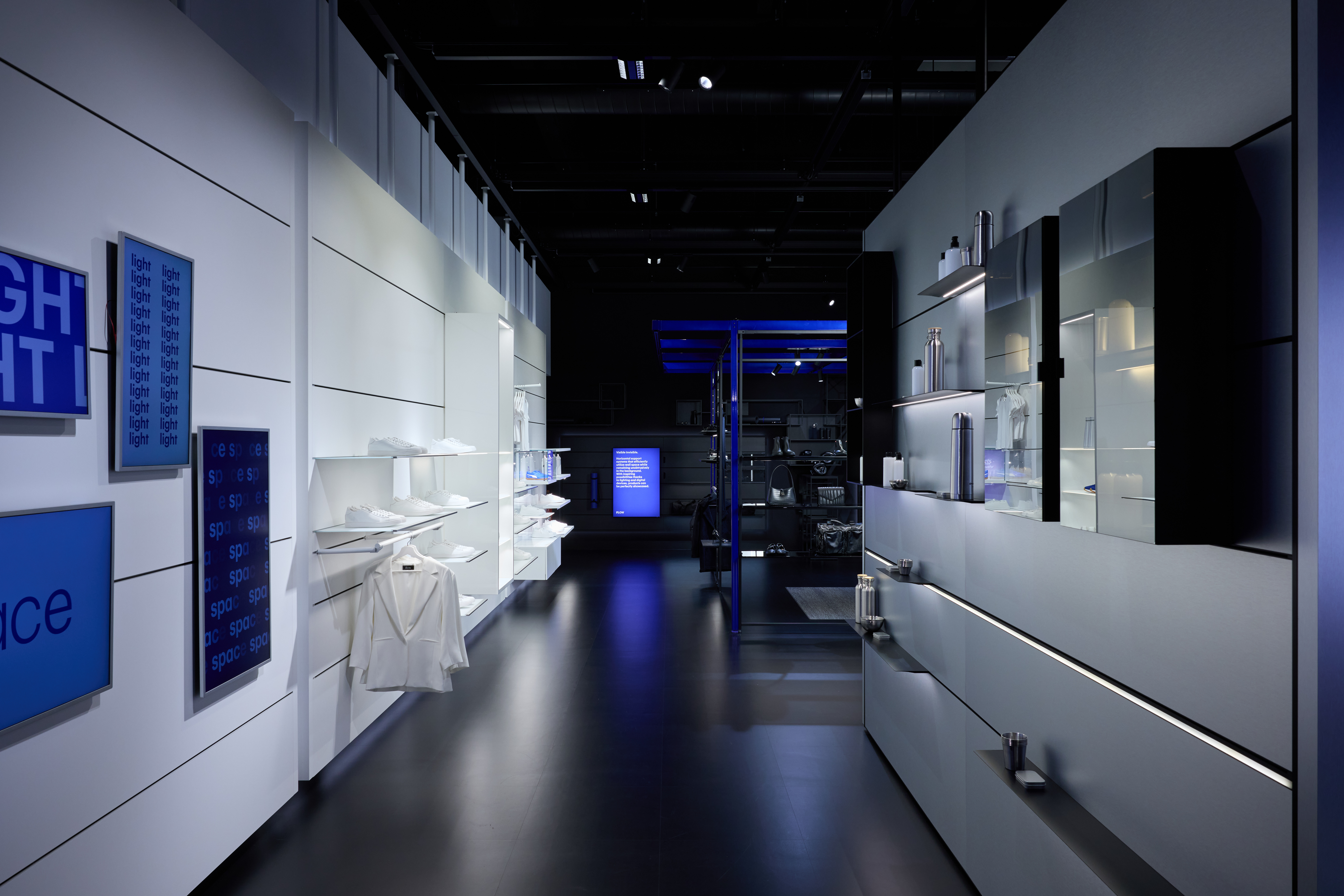 Modern showroom with modular black metal frames displaying clothing and accessories, illuminated by ceiling lights.