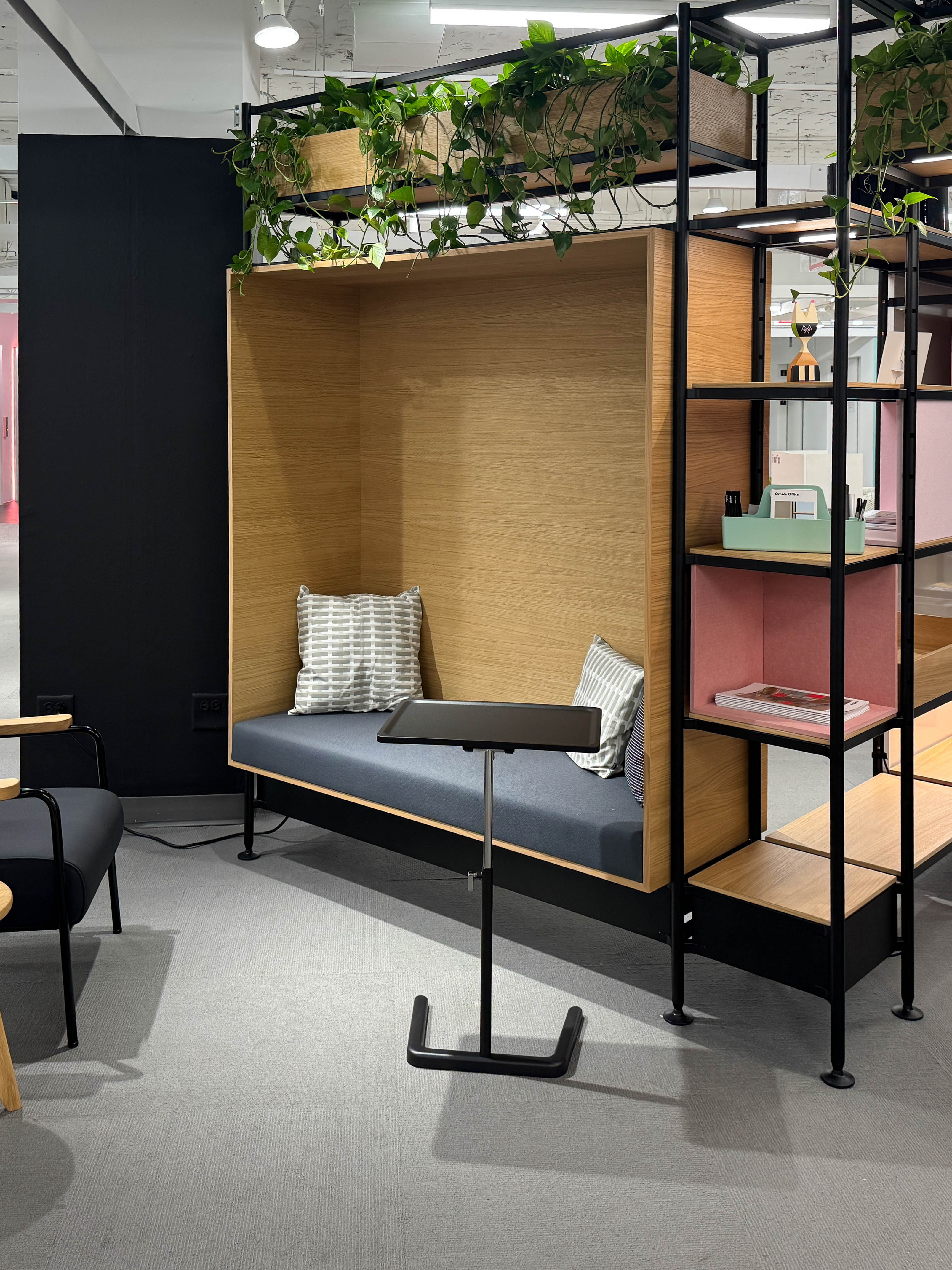 Wood-paneled seating nook with gray cushion, two patterned pillows, and black metal frame with shelves and plants.