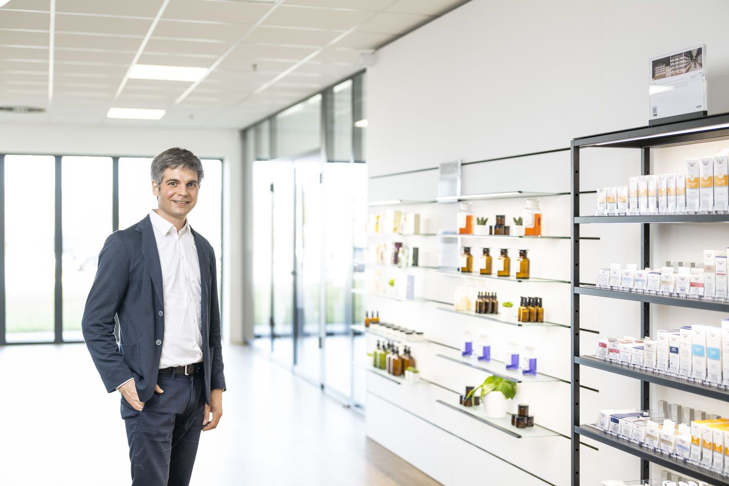 Ein Mann im Hemd gekleidet steht in einer hellen Apotheke.