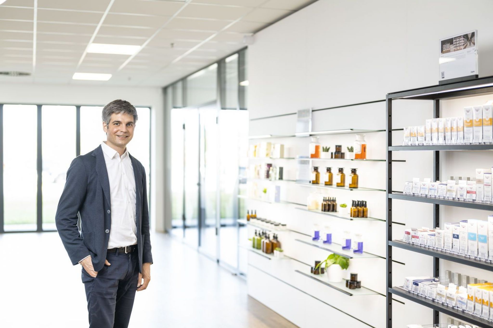 Ein Mann im Hemd gekleidet steht in einer hellen Apotheke.