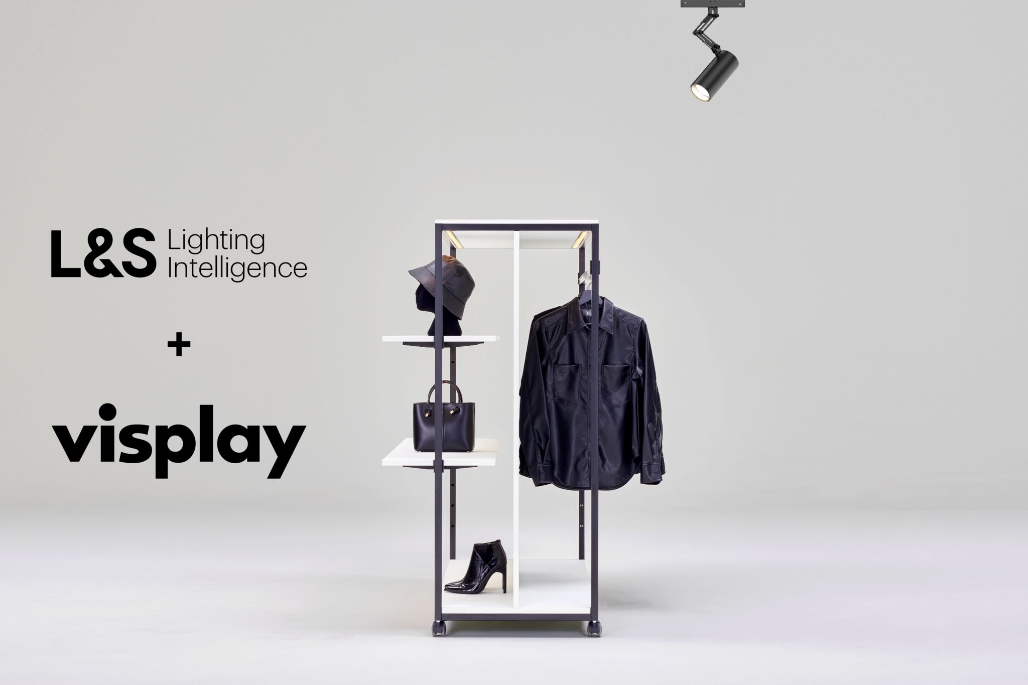 V&ecirc;tements et accessoires pr&eacute;sent&eacute;s sur une structure m&eacute;tallique noire minimaliste avec des &eacute;tag&egrave;res blanches, un seul spot noir au plafond, et les logos 'L&amp;S Lighting Intelligence' et 'visplay' &agrave; gauche.